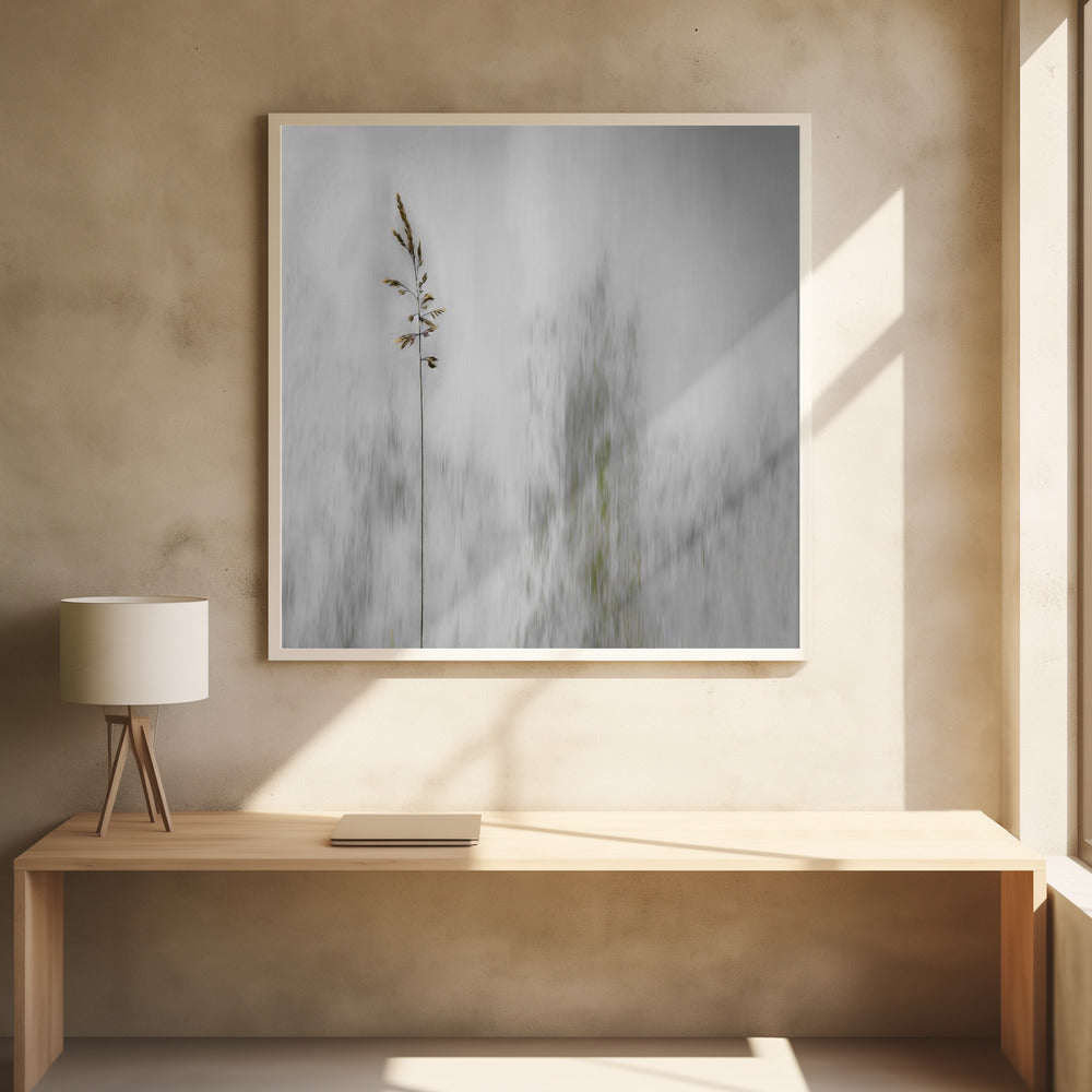 A minimalist photograph in a light wood frame featuring a single, delicate stalk of wild grass in sharp focus against a soft, vertically blurred background of gray and muted green tones, creating a tranquil and artistic impression. Print